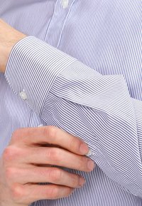 Skjorta med knappning fram som har tunna blå och vita vertikala ränder, med vikbara manschetter och pärlemorknappar på ärmarna.