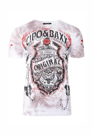 T-shirt en coton blanc avec imprimé graphique noir et rouge. Le design comprend un emblème avec du texte, des chaînes décoratives et des détails en éclaboussures abstraites.