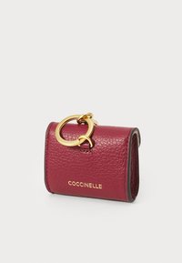 Red textured leather pouch featuring a gold hardware ring and a debossed logo on the front. Compact rectangular shape with contrasting edges.