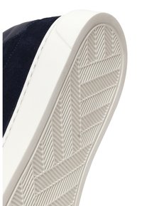 Close-up van de witte rubberen zool met chevronprofiel en marineblauwe suède bovenkant van een casual sneaker.