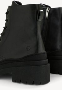 Bottes chevilles en cuir noir avec semelles épaisses à crampons, fermeture éclair latérale, languette arrière et lacets passés à travers des œillets en métal.
