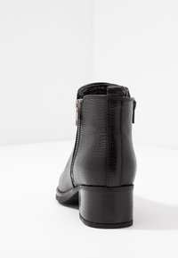 Botín negro de cuero hasta el tobillo con un acabado texturizado, cremallera lateral y tacón apilado, que presenta un diseño simple y elegante.