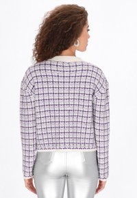 Lila és fehér kockás kötött pulóver, rövidített fazonnal, bordás nyakkal és hosszú ujjakkal, ezüst metallic nadrággal párosítva.