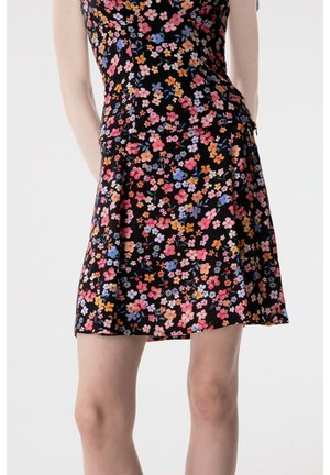 Gonna nera con stampa floreale piccola e colorata indossata da una persona, abbinata a una maglia a fiori coordinata, su uno sfondo bianco uniforme.