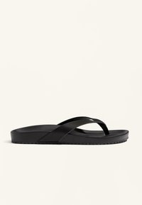 Sandal cu flip-flop negru, cu două bretele curbe, fabricat dintr-un material de cauciuc neted. Talpă plată cu un fund texturat pentru aderență. Design minimalist.