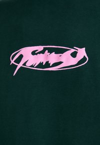 Mørkegrønn bomull T-skjorte med et fremtredende rosa grafisk logo i en flytende, kursiv stil innenfor en oval ramme.