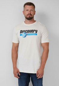 Cremfarbene Baumwoll-T-Shirt mit einem schwarzen und blauen "Discovery Channel"-Logo und einem Globusdesign, rundem Halsausschnitt und kurzen Ärmeln.