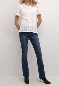 Vit stickad kofta med korta puffärmar, med en knappstängning och ett strukturerat mönster. Kombinerad med mörkblå slim-fit jeans och svarta ankelstövlar.