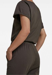 Mono gris de manga corta con un corte relajado, presenta escote redondo, cintura elástica y bolsillos laterales. Textura de tela suave y lisa.