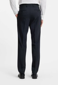 Pantaloni tailored navy con una texture liscia, doppie pinces e tasche posteriori. Rifiniti con una cintura e indossati con scarpe nere.