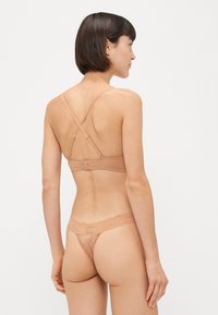 Beige bezdrátový bralet s krajkovými detaily, nastavitelné ramínka v křížovém designu, doplněný o odpovídající tangové kalhotky s krajkovým lemem.