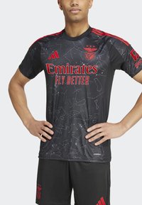 Juodas futbolo marškinėlis su raudonomis detalėmis ir logotipu "Emirates FLY BETTER". Modelis turi žvaigždžių formos raštus. Trumpomis rankovėmis, apvaliu kaklu.