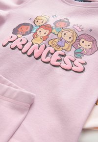 Sweatshirt rosa chiaro con una grafica a cartone animato di sei principesse, con testo bold rosa che legge "PRINCESS" sotto il design.