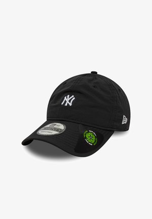 Black adjustable baseball cap with white "NY" logo on front and New Era logo on side, featuring two product stickers on the brim.