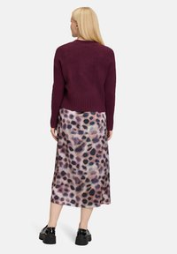 Bordeaux cropped sweater van zacht materiaal, gecombineerd met een lichtgewicht, gemêleerd midi-rok in zachte tinten en donkere vlekken. Zwarte platform schoenen.