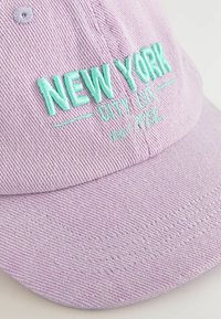 Lila baseballkeps med broderad "NEW YORK CITY LIFE" i ljusblått. Har textil med struktur och en rundad skärm.