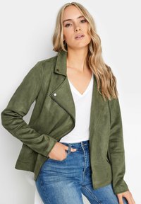 Olivgrön faux suede-jacka med asymmetrisk dragkedja, notch-krage och två sidofickor, i kombination med en vit V-ringad skjorta.