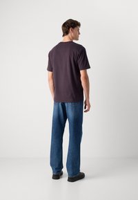 Rövid ujjú, sötétlila pamut póló, amit laza szabású kék farmernadrággal párosítottak. Az öltözet hétköznapi dizájnnal és kényelmes vonalvezetéssel rendelkezik.