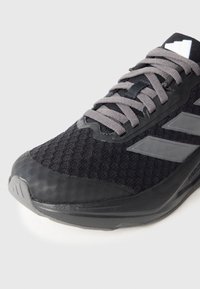 Čierna športová topánka vyrobená z meshu a syntetických materiálov, so sivými šnúrkami, tromi sivými pruhmi a tvarovanou špičkou.