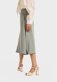 Gonna midi verde chiaro con un design fluido, abbinata a dei tacchi bianchi con cinturini caratterizzati da una trama intrecciata e un tacco spesso.