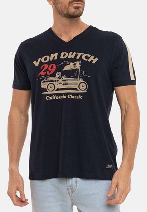 Homme portant un T-shirt bleu marine à col en V avec un graphisme de voiture vintage et un conducteur squelette, texte « VON DUTCH 29 California Classic ».
