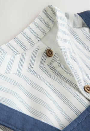 Hvidt stof med blå syede striber, brune knapper og en blå kant på en skjorte med krave.