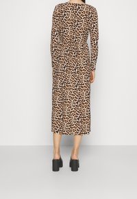 Vestido de manga larga con estampado de leopardo, cintura ceñida, de largo midi y tejido suave, combinado con zapatos de tacón grueso negros.