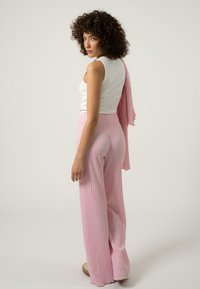 Pantalons larges à côtes roses avec une taille élastique, associés à un débardeur blanc ajusté. Le modèle porte une longue écharpe rose drapée sur son épaule.