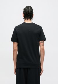 Μαύρο T-shirt με κοντά μανίκια, απαλό ύφασμα, λαιμόκοψη στρογγυλή, άνετη γραμμή, με εμφανείς ραφές, φορεμένο με χαλαρό μαύρο παντελόνι, εμφανίζει πλεξούδα στα μαλλιά.