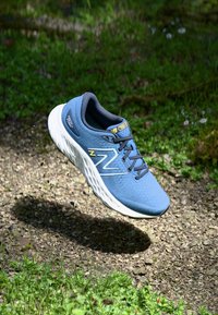 Chaussure de course bleue avec tige en mesh, semelle en mousse légère et accents jaunes. Elle dispose d'un nez arrondi et de détails de surface texturés.