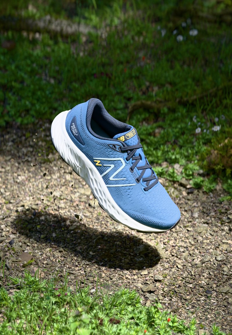 Chaussure de course bleue avec tige en mesh, semelle en mousse légère et accents jaunes. Elle dispose d'un nez arrondi et de détails de surface texturés.