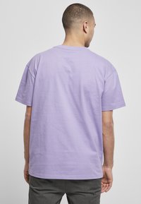 Tricou lejer din bumbac lavandă, cu mâneci scurte și decolteu rotund. Vederea din spate arată o textură netedă cu detalii simple de cusătură.