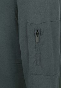 Donkergroene trui met een gebreide textuur, voorzien van een zak met rits op de mouw. De rits heeft een zwart treklipje voor gemakkelijke toegang.