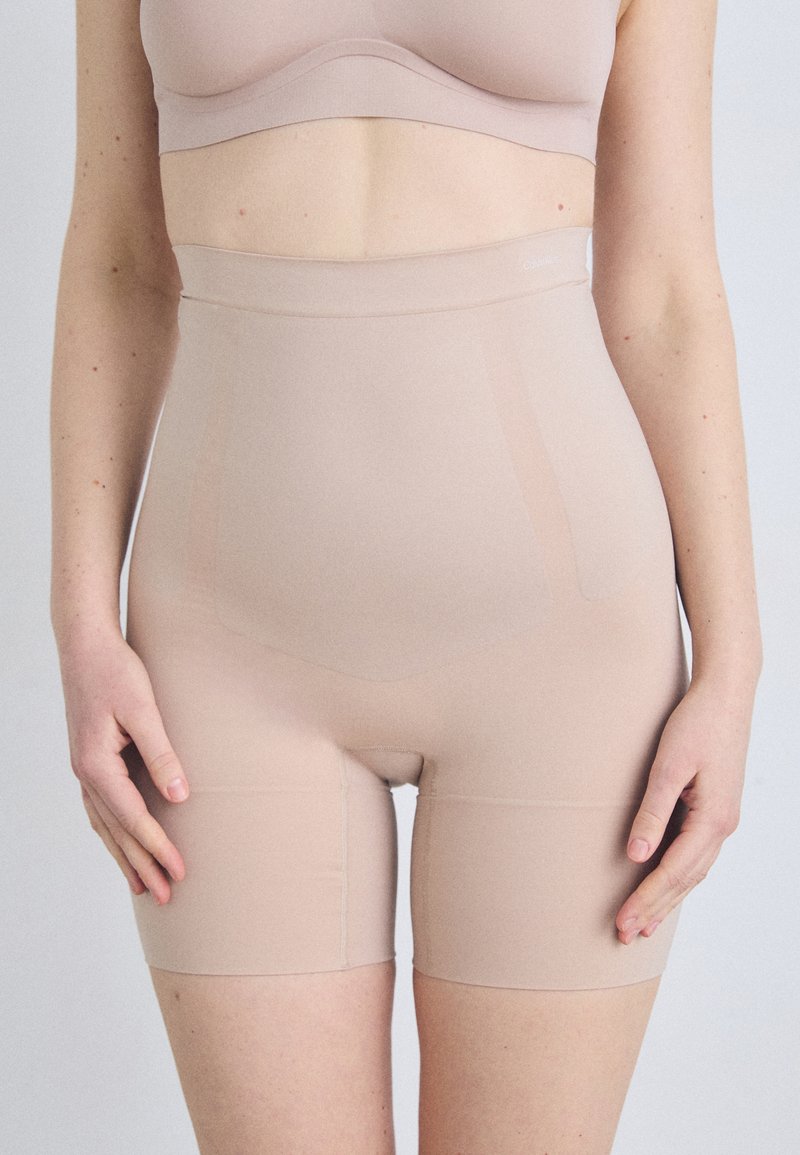 Beige high-waisted shapewear shorts van gladde, rekbare stof. Heeft een naadloos ontwerp en een snit tot halverwege de dij voor discrete gedragen.
