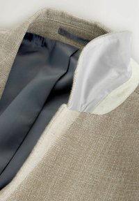 Kołnierz beżowej, teksturowanej kurtki podniesiony do góry, ukazujący gładką szarą podszewkę wewnętrzną oraz jasnoszary materiał pod kołnierzem.