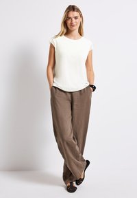 Lyscremfarvet kortærmet top med blondekant, parret med løstsiddende brune linnedbukser og sorte slip-on sko. Minimalistisk design.