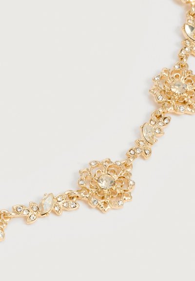 Χρυσό λουλουδάτο κολιέ με καθαρά στρας, οργανωμένα σε σχέδια λουλουδιών και φύλλων σε ανοιχτό φόντο.