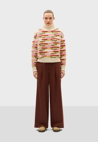 Maglione a righe con colletto alto, caratterizzato da motivi multicolori in rosa, verde e beige; abbinato a pantaloni larghi marroni e scarpe beige.