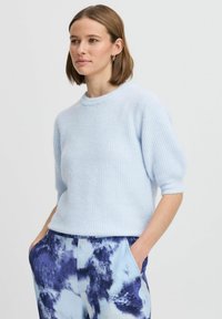 Helles blauer Rippstrickpullover mit Rundhalsausschnitt und Dreiviertelärmeln, kombiniert mit lockeren Hosen mit einem blau-weißen abstrakten Muster.