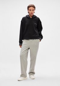 Musta huppari logolla ja harmaat collegehousut. Hupparissa on naru ja ribbatut hihansuut. Rentoa istuvuutta, pehmeä materiaali ja minimalistinen muotoilu.