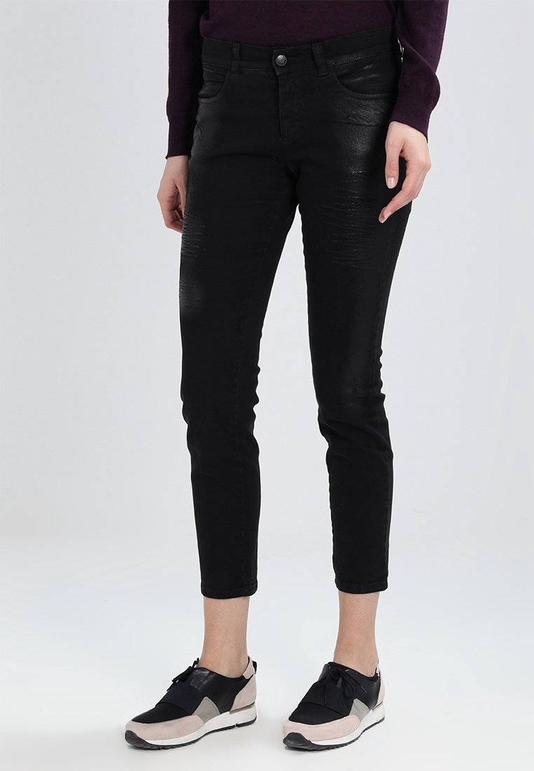 Personne portant un pantalon noir slim court avec des détails subtilement usés et des baskets décontractées noires et beiges.