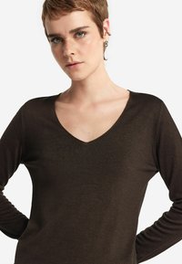 Brauner Langarmoberteil mit V-Ausschnitt und glatter Textur. Hat eine figurbetonte Silhouette und minimale Nahtdetails.