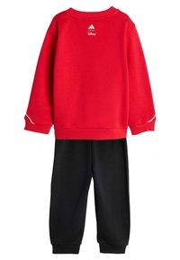 Crvena majica s bijelim detaljima i logotipom na dekolteu, u kombinaciji s crnim trenirkama koje imaju rebraste manžete.