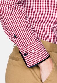 Punavalkoruudullinen paita, jossa on napitettava kalvosin, merivoimansinisiä yksityiskohtia ja pieni kirjailu. Yhdistetty vaaleanruskeisiin housuihin.