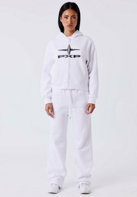 Witte hoodie met rits en zwart logo, gecombineerd met bijpassende joggingsbroek. Gladde, zachte stof met een relaxte pasvorm. Geen zichtbare patronen of accenten.