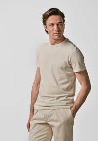 Beige katoenen t-shirt met korte mouwen, ronde hals en een ontspannen pasvorm. Subtiele textuur en stikseldetails verbeteren het eenvoudige ontwerp.