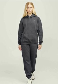 Sweatshirt cinza com capuz e bolso frontal, combinado com calças de treino coordendas. O tecido é macio e de textura suave. Design e ajuste simples.