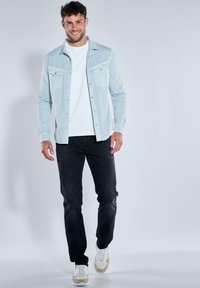 Light blue shirt with two chest pockets, paired with a white t-shirt, black jeans, and white sneakers with beige accents.
