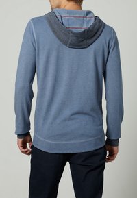 Sudadera azul de manga larga hecha de tela suave, con una capucha gris en capas que presenta un forro interno a rayas. Corte casual con puños acanalados.