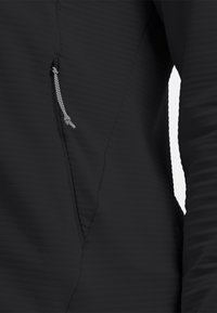 Black textured fabric top with a diagonal seam and zippered pocket, featuring a reflective cord pull detail on the zipper.
